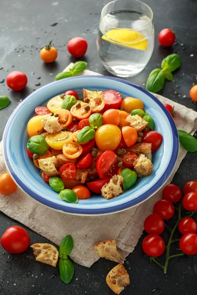 Panzanella Tomato salad with red, yellow, orange cherry tomatoes, capers, basil and ciabatta croutons. summer healthy food.