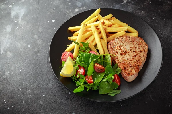 Bifes de atum frito na placa preta com verde fresco, salada de tomate, limão e batatas fritas. alimento saudável para o mar — Fotografia de Stock