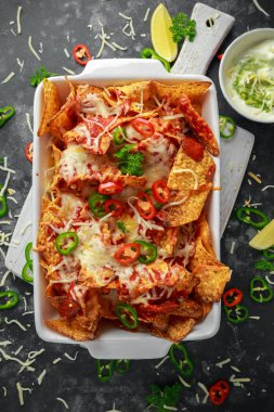 Maxican tarzı tortilla cips cips domates salsa ile tepesinde, dilimlenmiş chilies ve eritilmiş peynir servis limon dilimleri ve avokado yoğurt sos ile