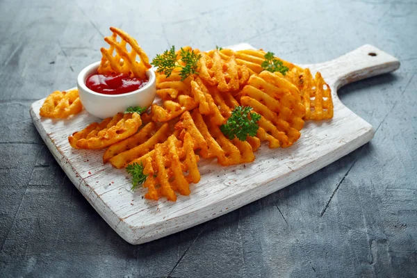 Crispy Potato Waffles Fries with Ketchup on white wooden board.