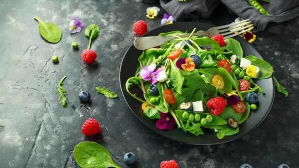 Summer salad with edible flowers, spinach, blueberries, raspberry, sweet peas, cherry tomatos and feta cheese
