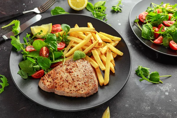 Bifes de atum frito na placa preta com verde fresco, salada de tomate, limão e batatas fritas. alimento saudável para o mar — Fotografia de Stock