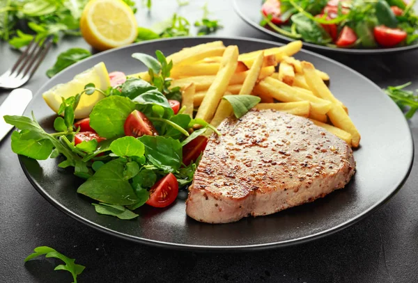 Rántott tonhal steak a fekete tányér paradicsom saláta, citrom, friss zöld, hasábburgonyával. egészséges tengeri ételek — Stock Fotó