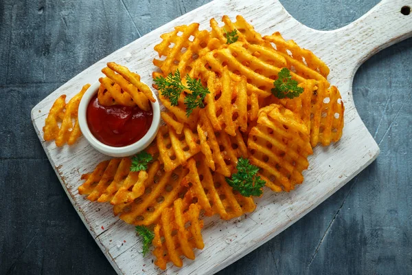 Crispy Potato Waffles Fries with Ketchup on white wooden board