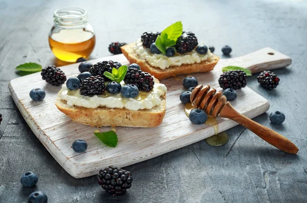 Świeże jeżyny słodkiej, Blueberry bruschetta, Grzanka z serem, miód w biały deska. — Zdjęcie stockowe