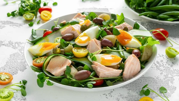 Gezonde Nicoise salade met zalm, kleurrijke sweet cherry tomaten, olijven, groene bonen, komkommer linten, zacht gekookte eieren, water-tuinkers verlaat met mediterrane kruiden Stockfoto