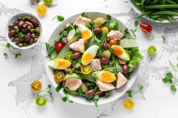 Gezonde Nicoise salade met zalm, kleurrijke sweet cherry tomaten, olijven, groene bonen, komkommer linten, zacht gekookte eieren, water-tuinkers verlaat met mediterrane kruiden Rechtenvrije Stockfoto's