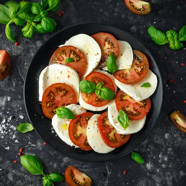 Salada Caprese com tomate, queijo mussarela e folhas de manjericão fresco em um prato preto. Comida italiana . — Fotografia de Stock