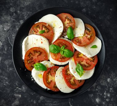 Caprese salatası domates, mozzarella peyniri ve taze fesleğen ile siyah bir tabak içinde bırakır. Italyan Mutfagi.