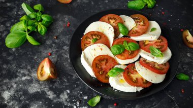 Caprese salatası domates, mozzarella peyniri ve taze fesleğen ile siyah bir tabak içinde bırakır. Italyan Mutfagi.