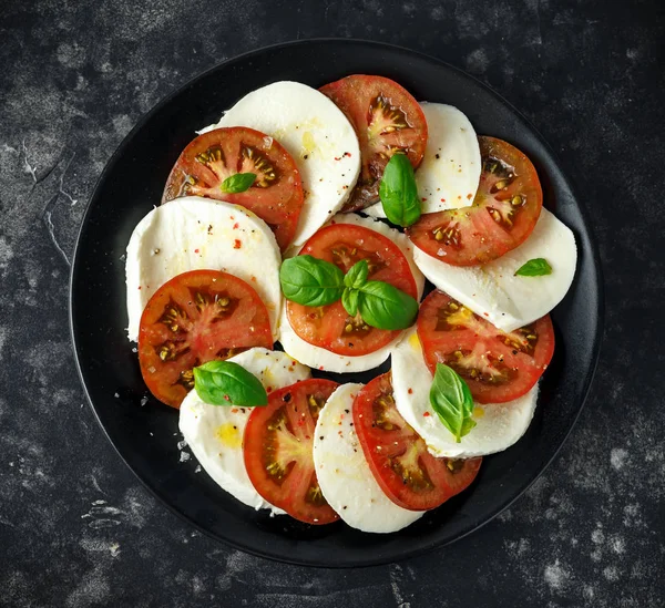 Caprese salatası domates, mozzarella peyniri ve taze fesleğen ile siyah bir tabak içinde bırakır. Italyan Mutfagi. — Stok fotoğraf