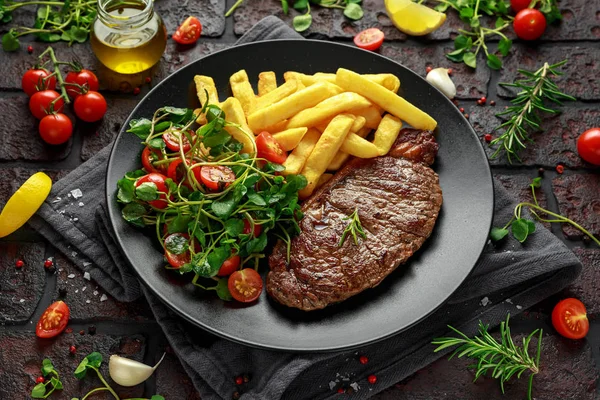 サーロイン ステーキ ポテト フライと野菜、トマトのサラダ黒プレートで。素朴なテーブル — ストック写真