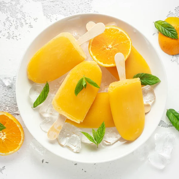 Picolés, piruetas de gelo em pau com suco de laranja doce em placa branca com gelo — Fotografia de Stock