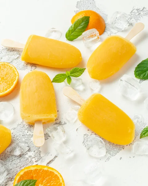 Paletas, paletas de hielo en palo con zumo de naranja dulce sobre fondo blanco con hielo —  Fotos de Stock