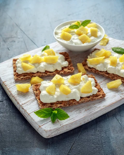 Tostadas caseras de pan crujiente con queso Cottage y piña sobre tabla de madera blanca . —  Fotos de Stock