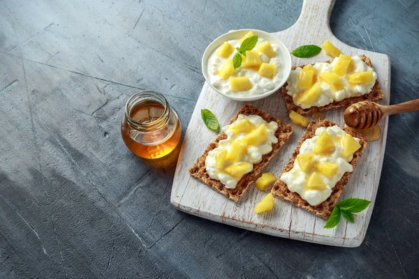 Süzme peynir, ananas ve beyaz ahşap tahta üzerinde bal ile ev yapımı Crispbread ekmeği.