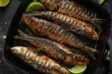 Izgara sardalya dökme demir tava üzerinde kekik, biber ve limon dilimleri ile