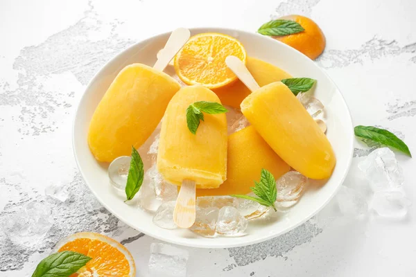 Picolés, piruetas de gelo em pau com suco de laranja doce em placa branca com gelo — Fotografia de Stock