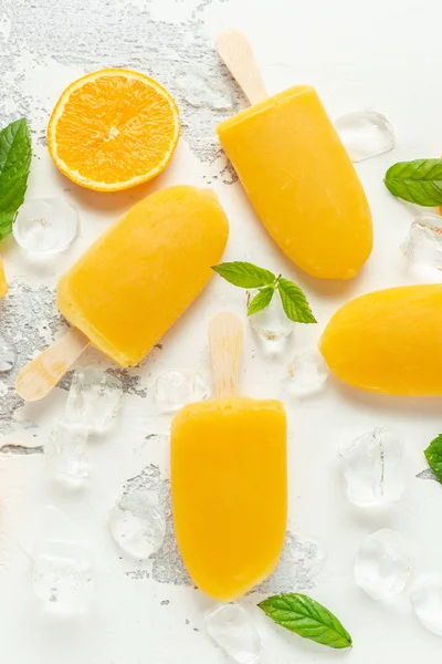 Picolés, piruetas de gelo em pau com suco de laranja doce no fundo branco com gelo — Fotografia de Stock