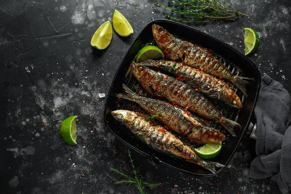 Grillade sardiner med timjan, chili och lime kilar på gjutjärn stekpanna — Stockfoto