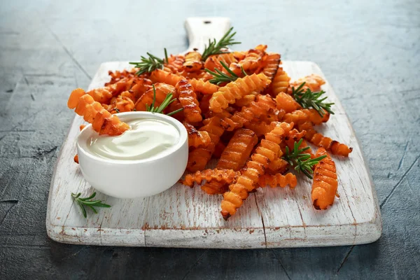 Baked butternut squash fries with sea salt and rosemary. Pumpkin chips on white wooden board.