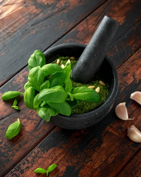 Green Basil Pesto em argamassa de mármore com queijo parmesão, pinhões, alho e limão sobre fundo rústico de madeira — Fotografia de Stock