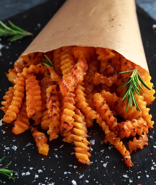 Baked butternut squash fries with sea salt and rosemary in paper cone. Pumpkin chips