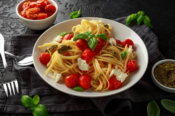 Pasta al pesto verde, pomodorini arrosto e mozzarella in piatto bianco su fondo rustico scuro — Foto Stock