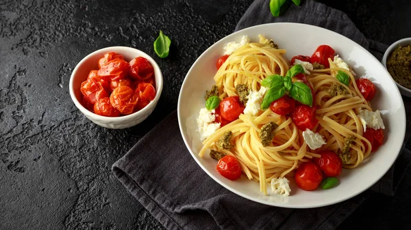 Pasta mit grüner Pesto-Sauce, gerösteten Kirschtomaten und Mozzarella in weißem Teller auf dunklem rustikalem Hintergrund — Stockfoto