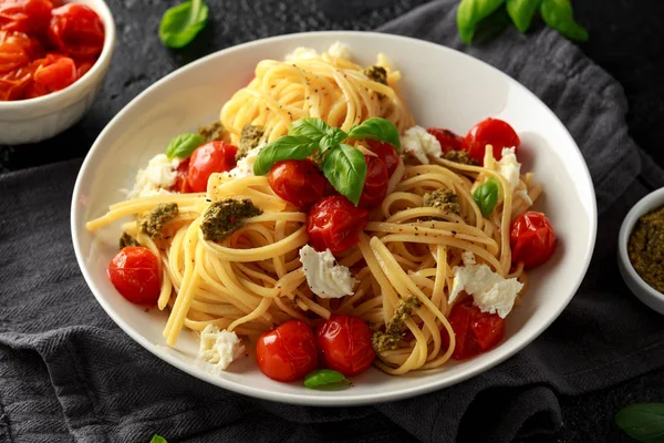 Pasta al pesto verde, pomodorini arrosto e mozzarella in piatto bianco su fondo rustico scuro — Foto Stock