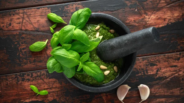 Green Basil Pesto em argamassa de mármore com queijo parmesão, pinhões, alho e limão sobre fundo rústico de madeira — Fotografia de Stock