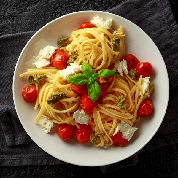 Massa com molho pesto verde, tomate cereja torrado e queijo mussarela em placa branca sobre fundo rústico escuro — Fotografia de Stock