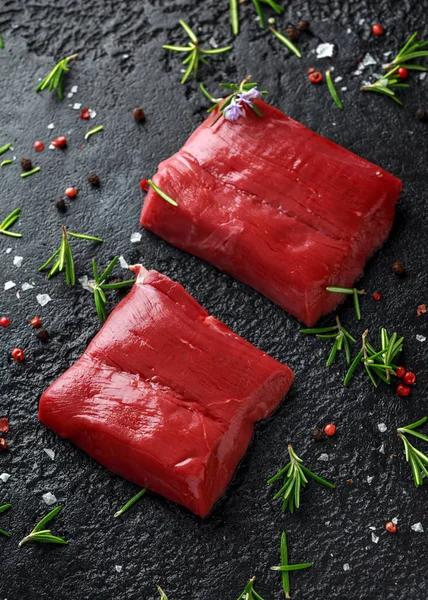 Filete de venado crudo con romero y pimienta sobre mesa rústica negra . — Foto de Stock