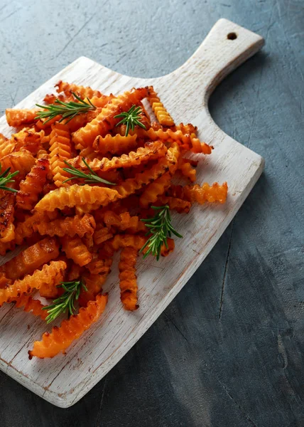 Baked butternut squash fries with sea salt and rosemary. Pumpkin chips on white wooden board.