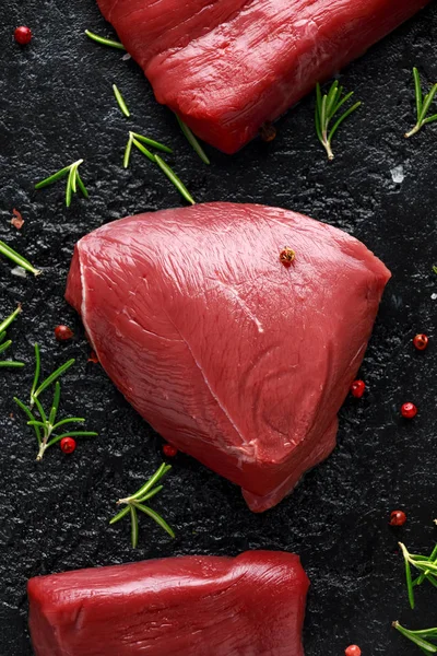 Filete de venado crudo con romero y pimienta sobre mesa rústica negra . — Foto de Stock