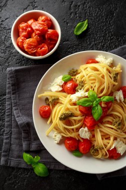 Yeşil pesto sos, Közlenmiş Domates ve mozzarella peyniri rustik koyu arka plan üzerinde beyaz plaka ile makarna