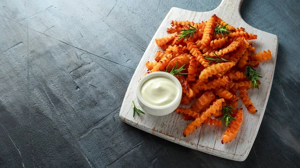 Baked butternut squash fries with sea salt and rosemary. Pumpkin chips on white wooden board.