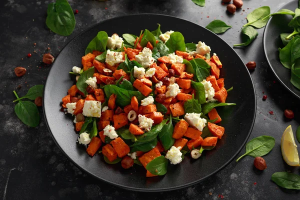 Frisk ristet søtpotetsalat med spinat, fetaost, hasselnøtter i svart tallerken – stockfoto