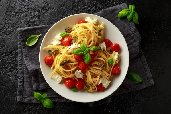 意大利面配绿色香菜酱、烤樱桃西红柿和在黑暗质朴背景的白色盘子里的马苏雷拉奶酪 — 图库照片