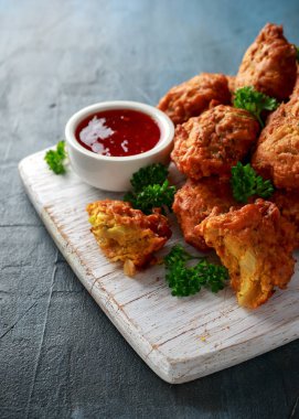 Crispy onion bhajis with sweet chilli sauce on white wooden board clipart