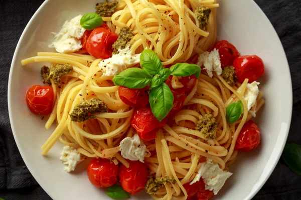 Pasta con salsa pesto verde, tomates cherry asados y queso mozzarella en plato blanco sobre fondo rústico oscuro —  Fotos de Stock