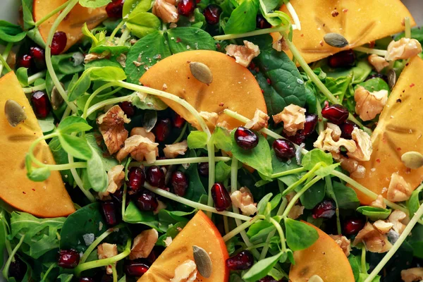 Sabrosa ensalada de caqui y guisantes con nueces, granada y semillas de calabaza en un plato blanco —  Fotos de Stock