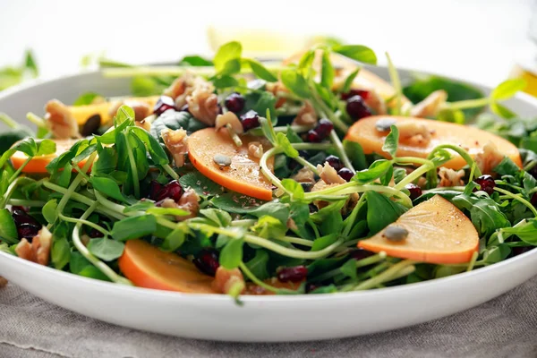 Tasty Persimmon and pea shoot salad with walnuts, pomegranate and pumpkin seed in a white plate — Stock Photo, Image