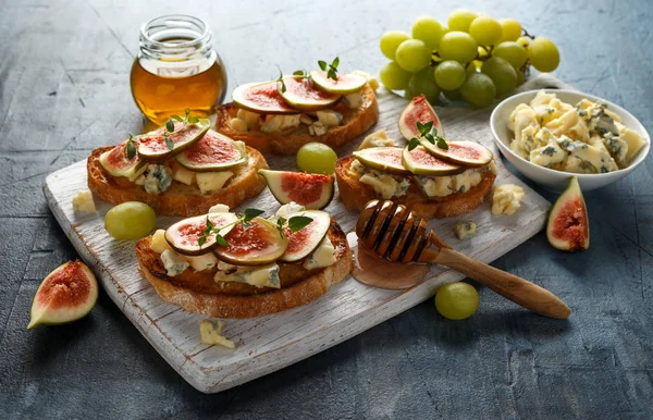 Estas tartinas de higo y gorgonzola, tostadas, bruschetta. rociado con miel sobre tabla de madera blanca —  Fotos de Stock