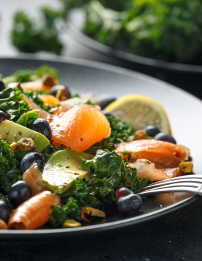 Somon Kale süper yiyecek salata avokado, Antep fıstığı ve siyah plaka üzerinde yaban mersini