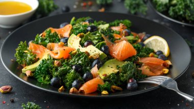 Somon Kale süper yiyecek salata avokado, Antep fıstığı ve siyah plaka üzerinde yaban mersini