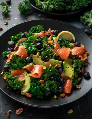 Somon Kale süper yiyecek salata avokado, Antep fıstığı ve siyah plaka üzerinde yaban mersini