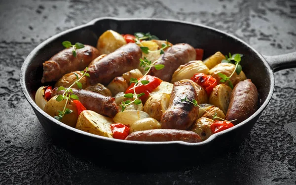 Patates, kırmızı biber ve soğan rustik demir Pan ile ev yapımı domuz sosisi