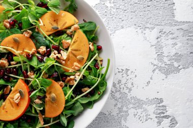 Trabzon hurması ve bezelye salatası ceviz, nar ve kabak çekirdeği beyaz bir tablo içinde ateş.