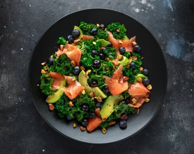 Somon Kale süper yiyecek salata avokado, Antep fıstığı ve siyah plaka üzerinde yaban mersini